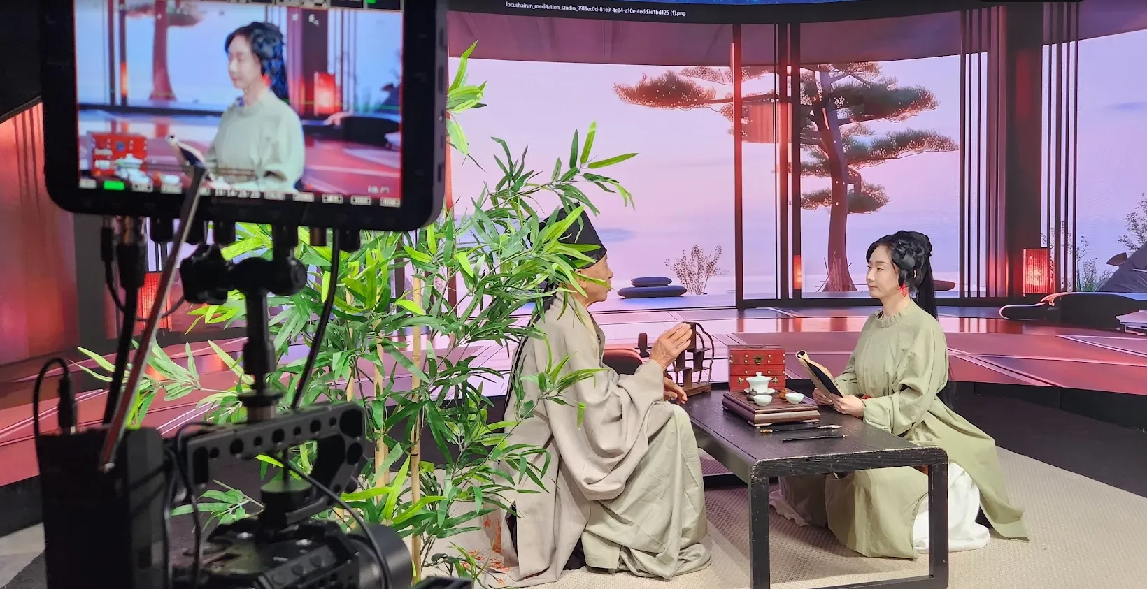 Two actors in traditional robes at tea table with bamboo and LED pavilion background, Upperland Studio