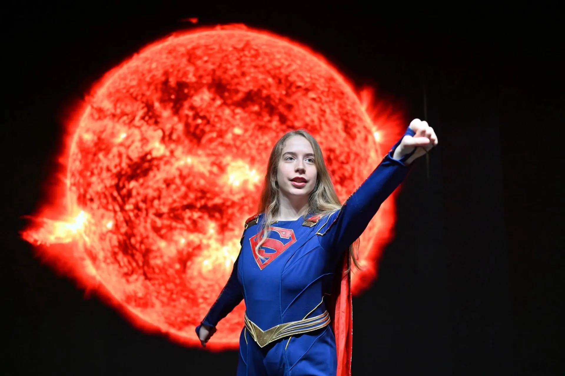 Supergirl portrait with a raised arm and solar imagery