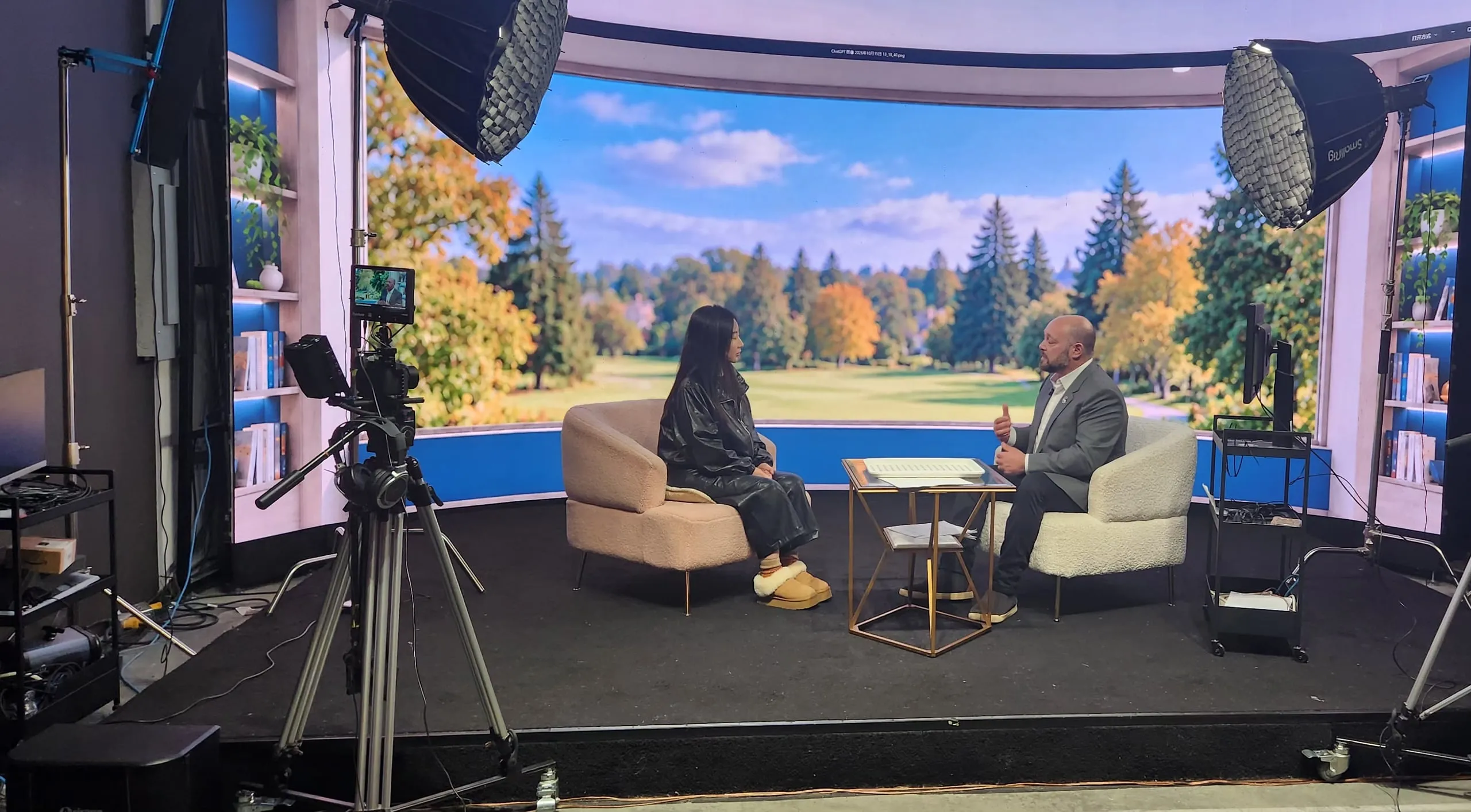 Wide view of Sarah Yu interviewing Jaime Stein, with cameras, lights and autumn LED scenery