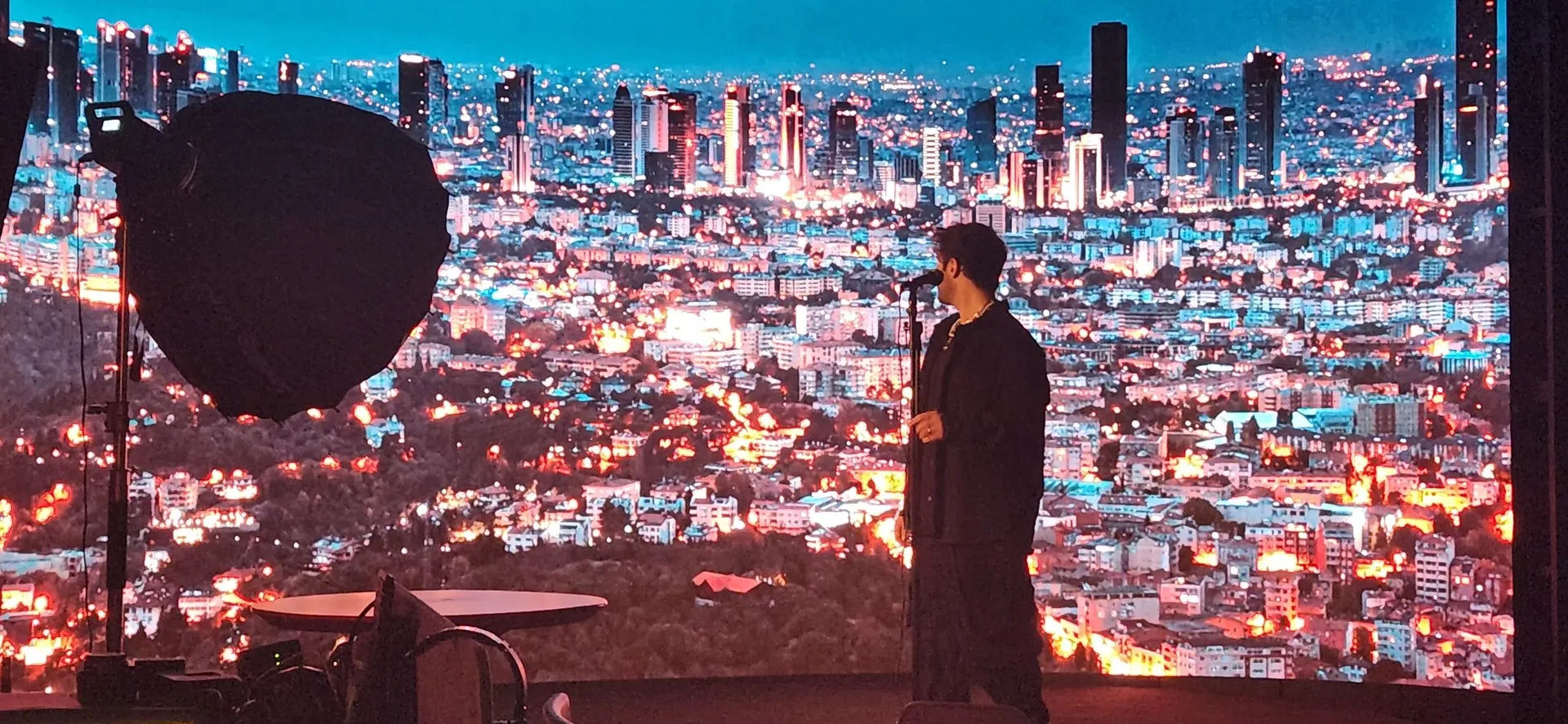 Side view of the performer and microphone against a city-night scene