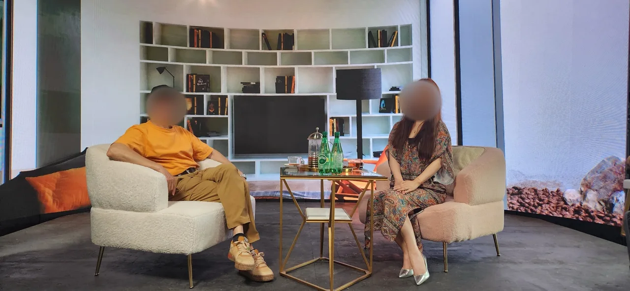 Man and woman in conversation on armchairs before a living-room LED backdrop