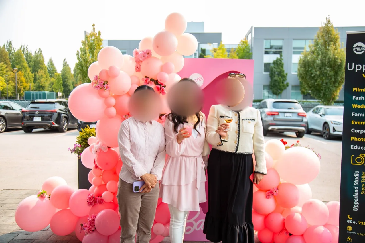 Three guests with drinks at the Barbie balloon arch outside the studio
