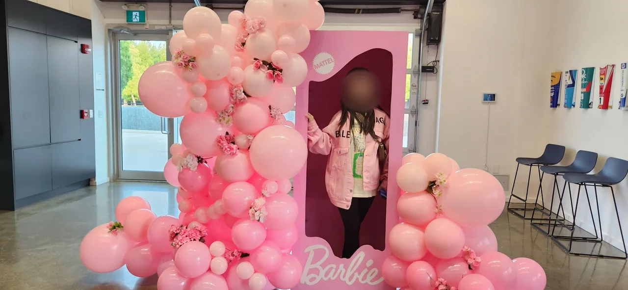 Guest in a pink jacket posing inside the Barbie photo box with balloon arch