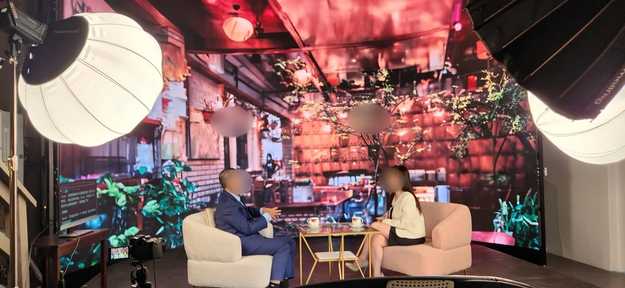 Host interviewing a guest in a suit before a garden café LED backdrop with studio lights