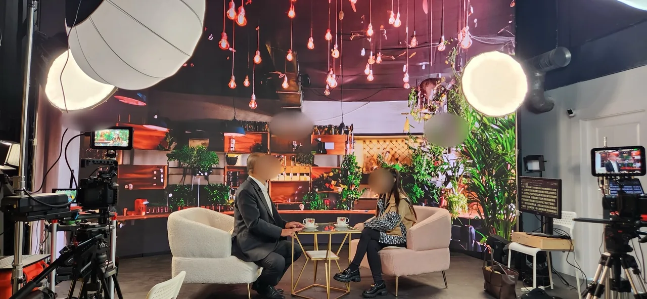 Two-camera interview setup with café LED backdrop and hanging bulb lights