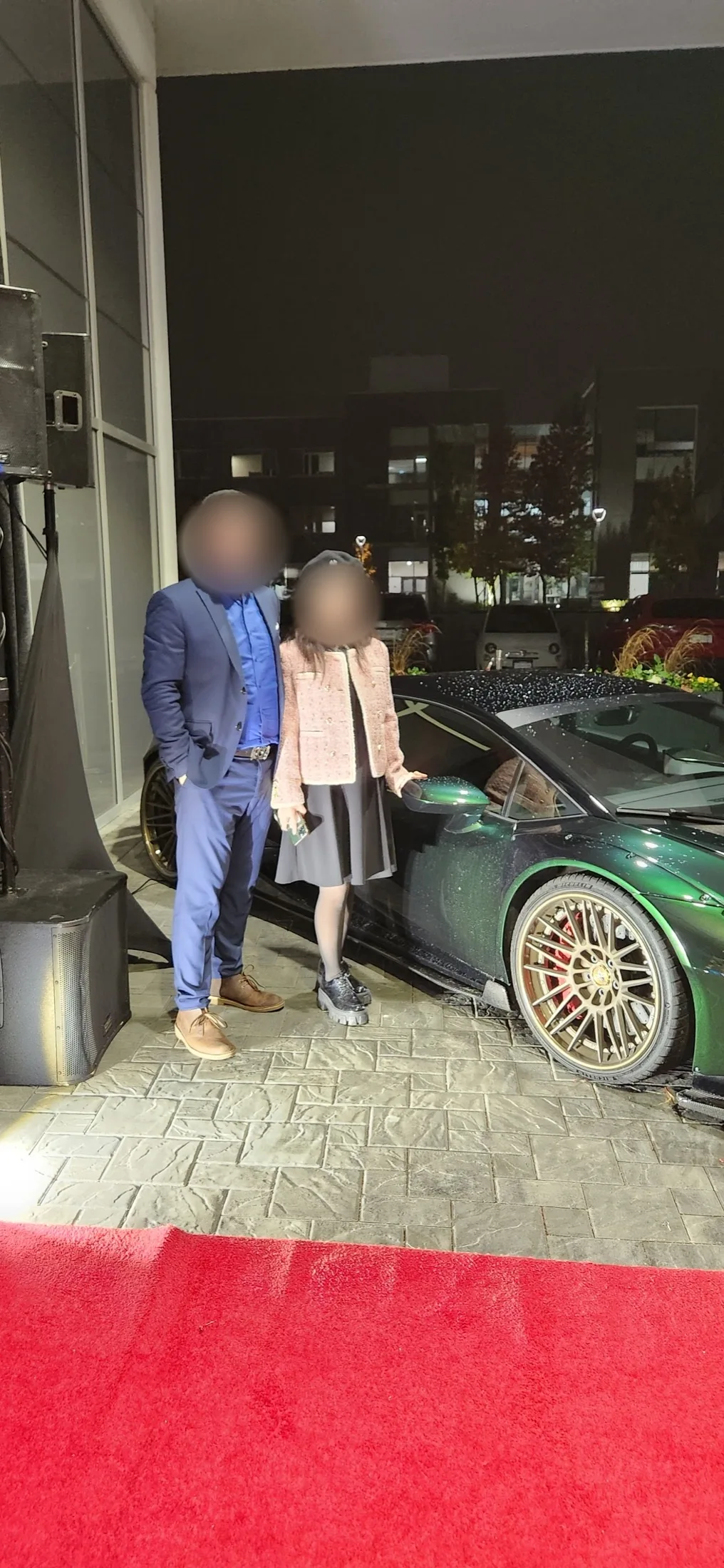 Guests posing with a green Lamborghini on the red carpet at night