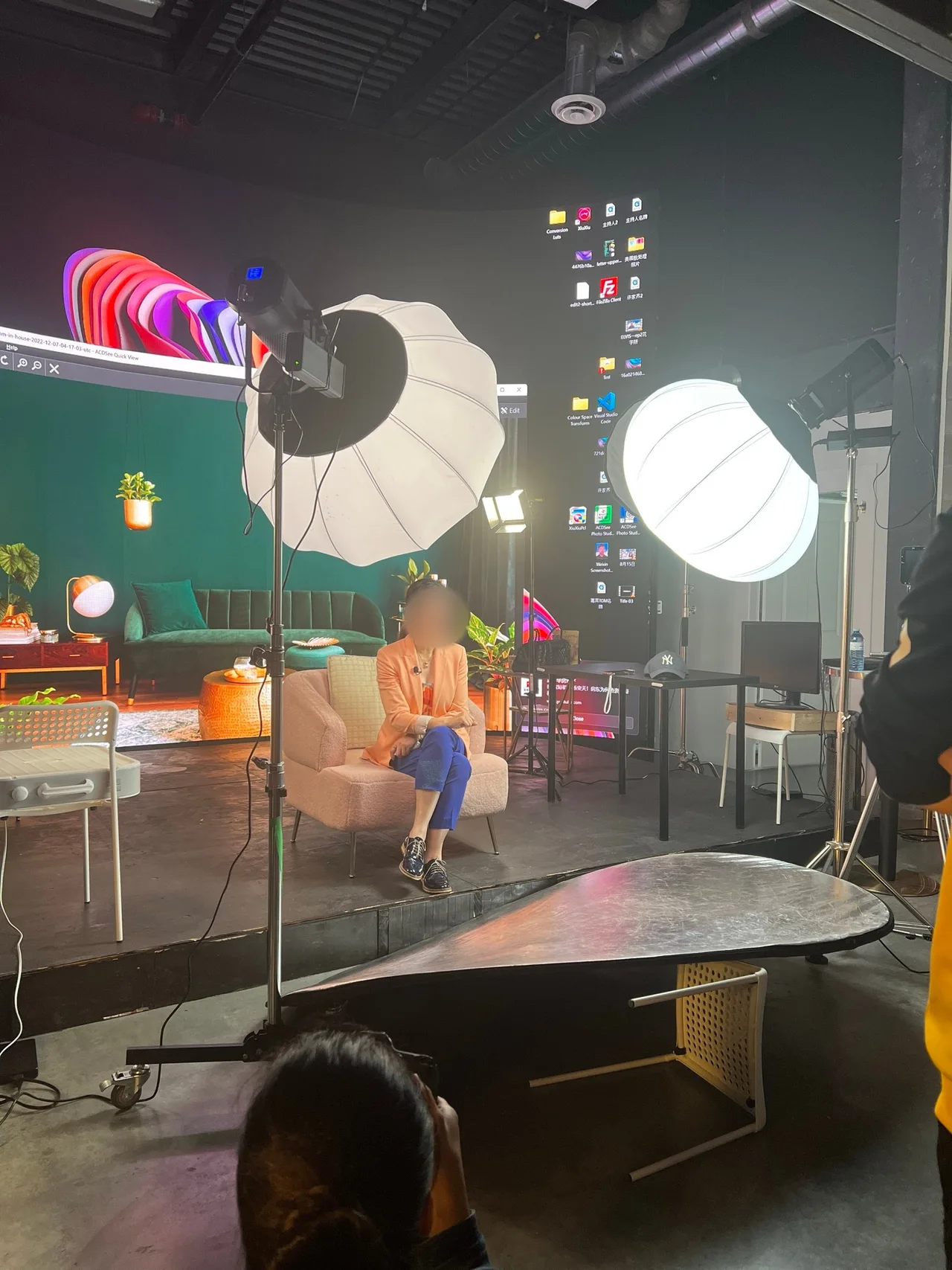 Guest in a peach blazer seated for an interview before a green living-room LED backdrop
