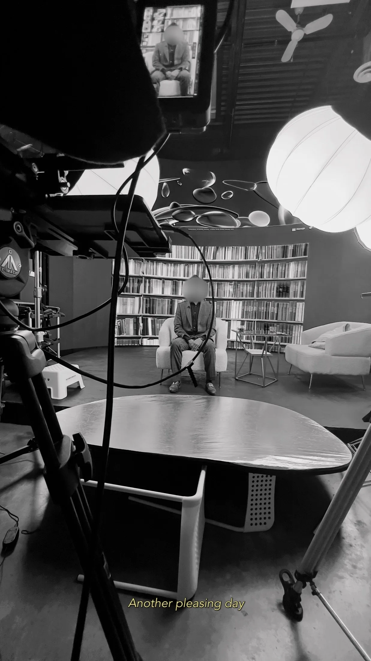 Black-and-white BTS of a guest recording an interview before a bookshelf LED backdrop