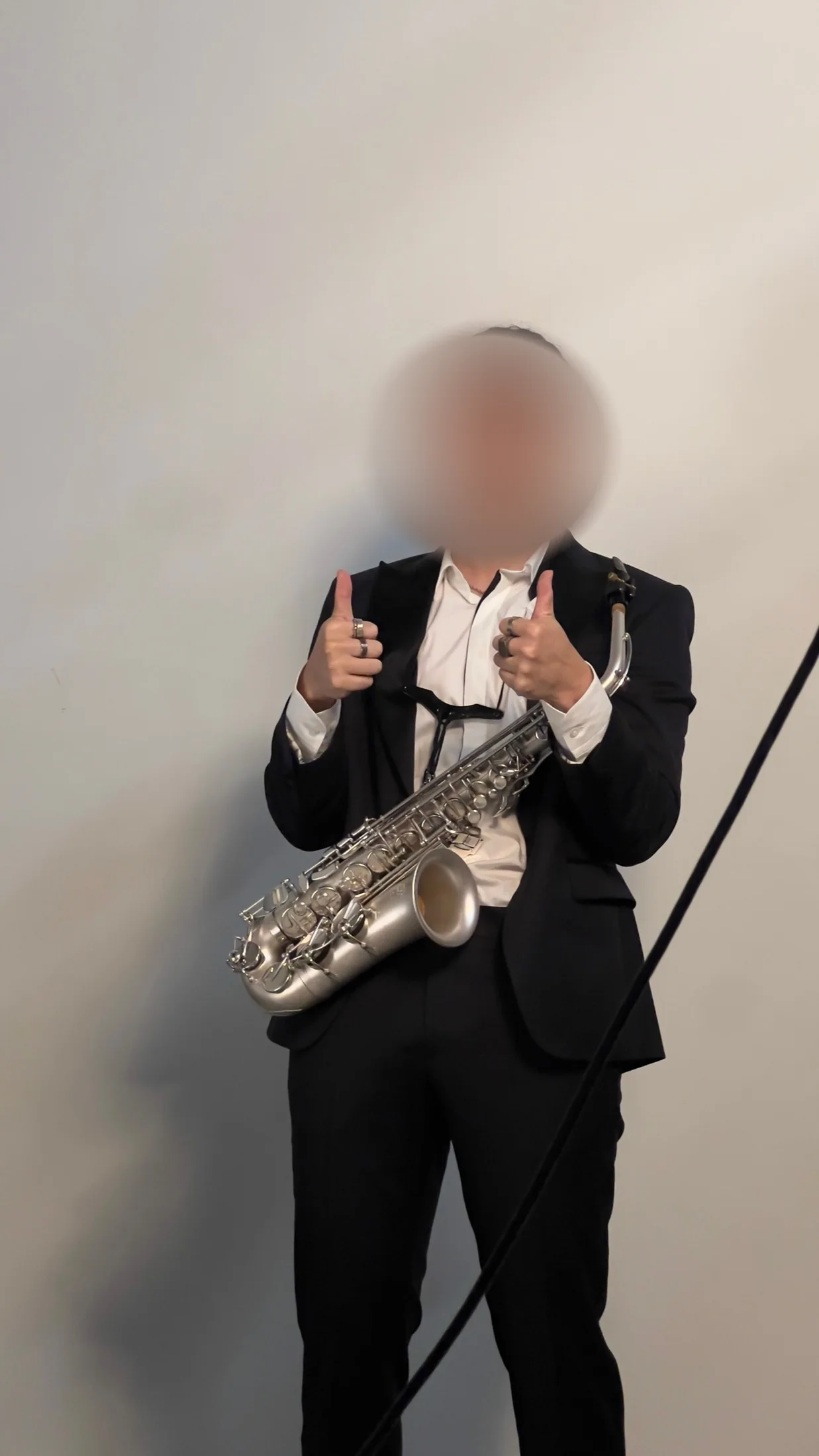 Saxophonist in a suit holding a silver saxophone, giving two thumbs up