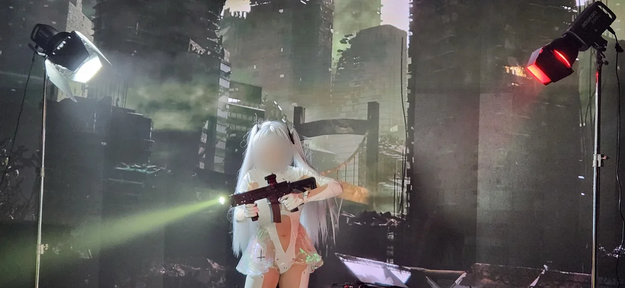 White-haired cyberpunk cosplayer holding a laser prop gun in front of a ruined cityscape backdrop on the LED wall at Upperland Studio, Richmond BC