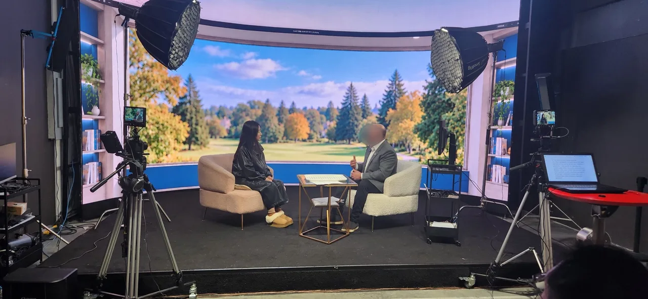 Wide behind-the-scenes view of the interview set with two cameras and an autumn park LED backdrop