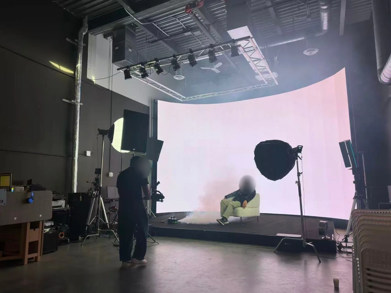 Singer seated alone on a cream sofa against an all-white LED wall with low dry-ice fog, filmed on a gimbal during the Route 66 Films shoot at Upperland Studio