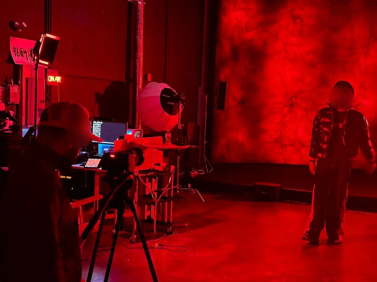 Behind-the-scenes photo of the singer performing against a red cracked-texture LED wall in full red light, camera on tripod and video village to the left