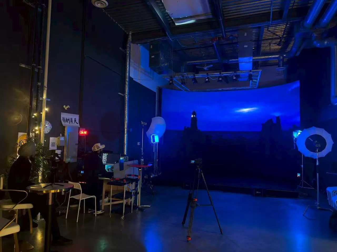 The curved LED wall at Upperland Studio displaying a deep-blue night sea and lighthouse virtual set during the Route 66 Films music video production, camera on tripod in the foreground