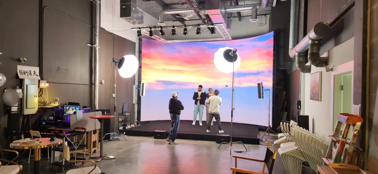 Wide behind-the-scenes view of the Route 66 Films Punjabi music video at Upperland Studio, lead actors performing in front of a curved LED wall showing a pink and orange sunset sky