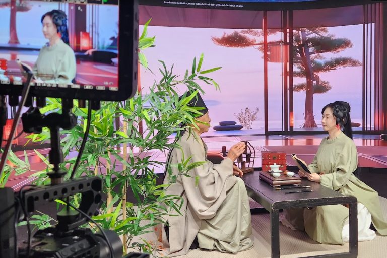 Two actors in traditional robes at tea table with bamboo and LED pavilion background, Upperland Studio